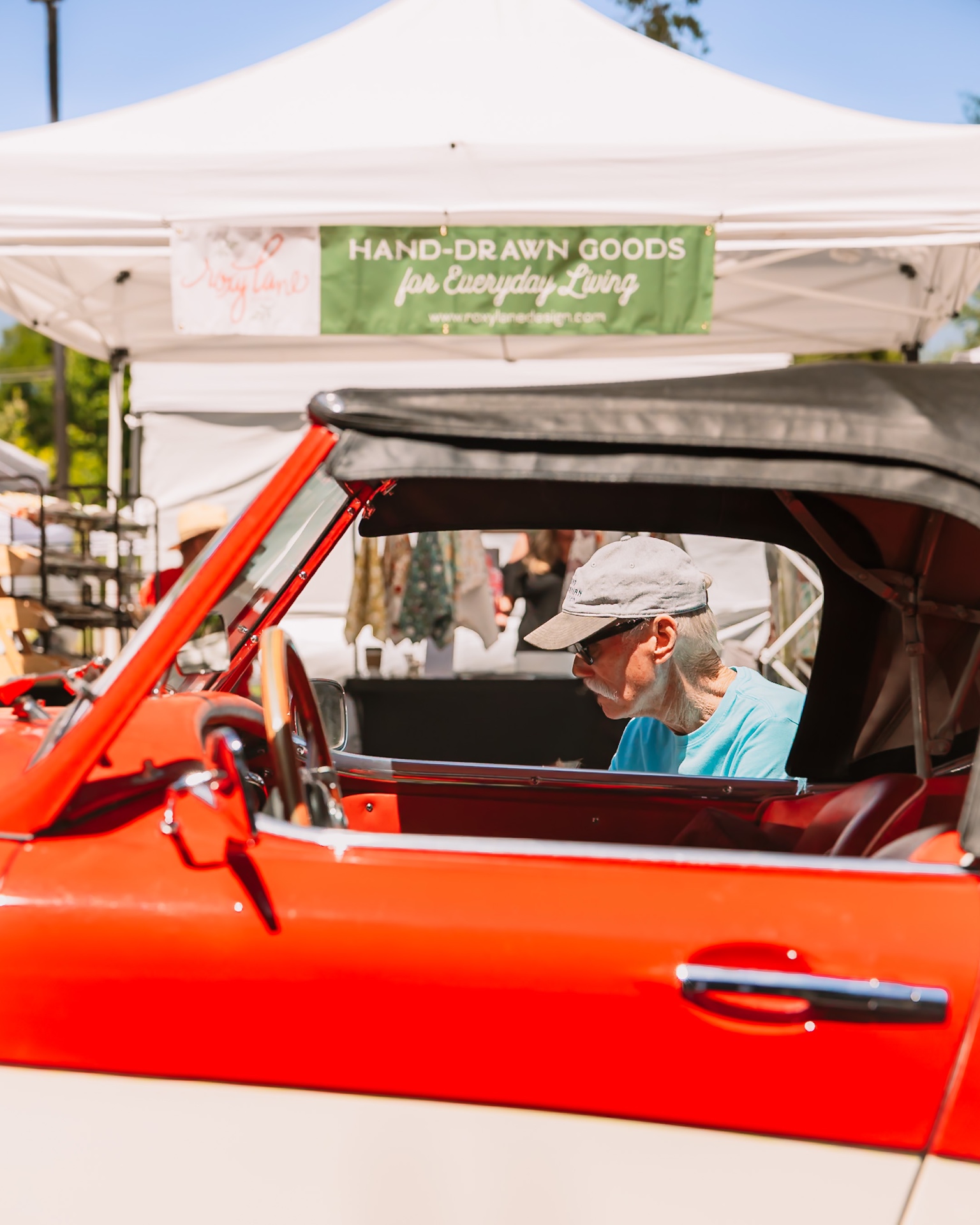 Owner seated in a red British convertible at the market