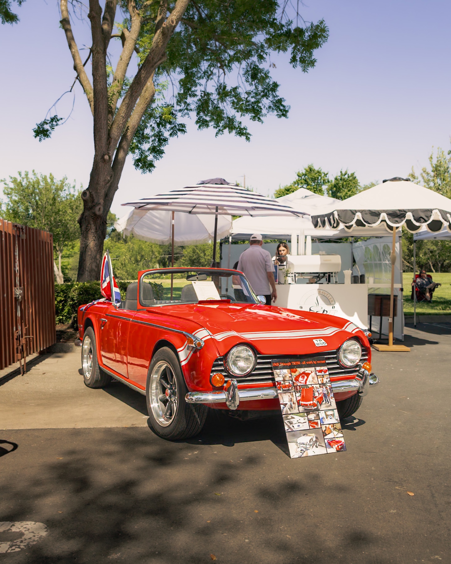 Red 1968 Triumph TR250 with Union Jack flag parked beside market coffee stand